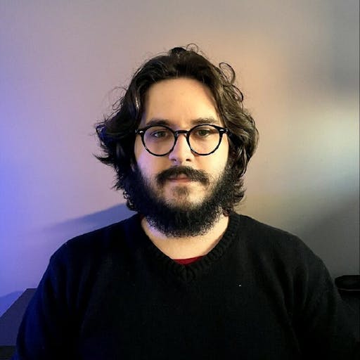 Minha foto de perfil que vai do topo da cabeça até a altura do ombro, estou com cabelo e barba curtos, vestindo um óculos e uma blusa de moletom azul